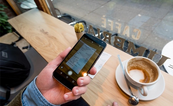 Hand holding phone with receipt and coffee